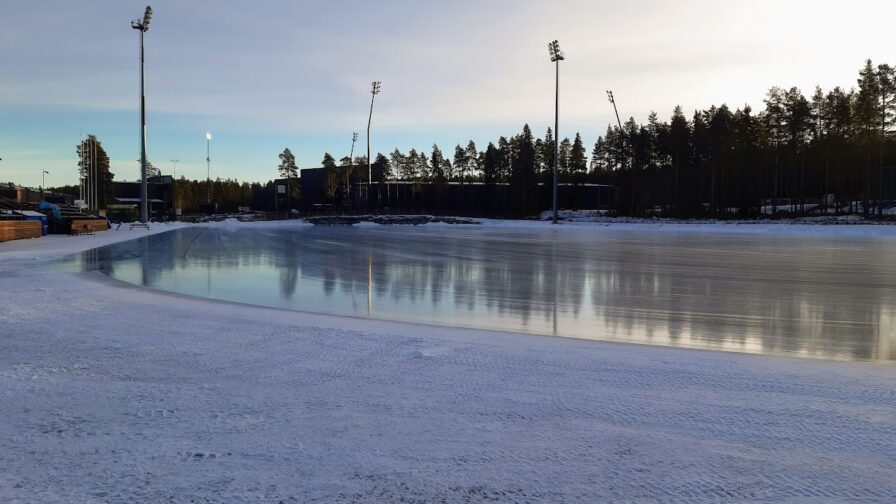 Jäädytetty iso tekojääkenttä. Taustalla puita ja jalkapallostadion.