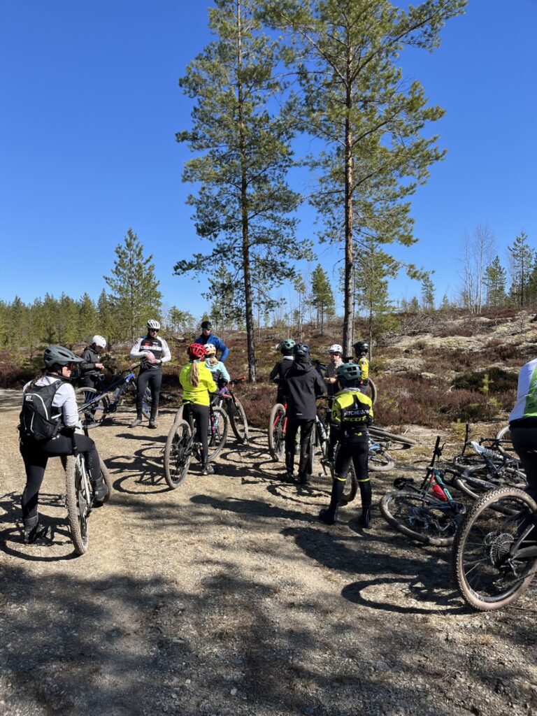 Nuoria pyöräilijöitä tauolla pitkällä peruskuntolenkillä hiekkatiellä. Taustalla metsää ja kallio.