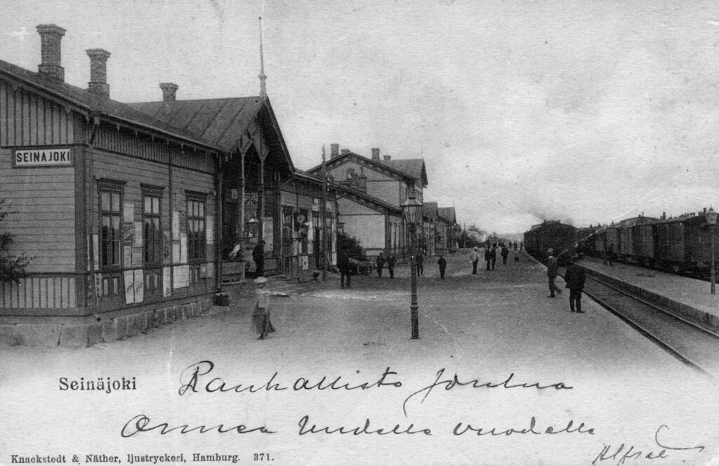 Mustavalkoisessa kuvassa vanha asemarakennus ja teksti rauhallista joulua ja onnea uudelle vuodelle