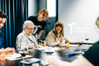 Ihmisiä pöydän ääressä maalaamassa