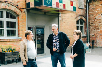 Kolme henkilöä keskustelee tiilirakennuksen edustalla