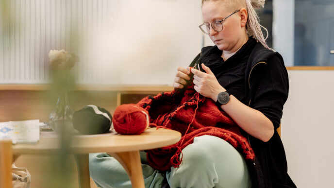 henkilö istuu tuolilla risti-istunnassa ja neuloo villavaatetta