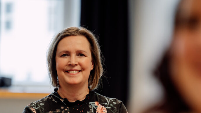 hymyilevä, istuva henkilö katsoo suoraa kameraan