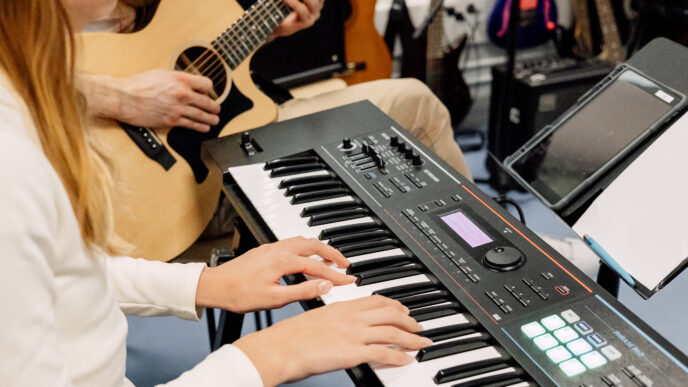 henkilö soittaa pianoa ja taustalla toinen henkilö kitaraa