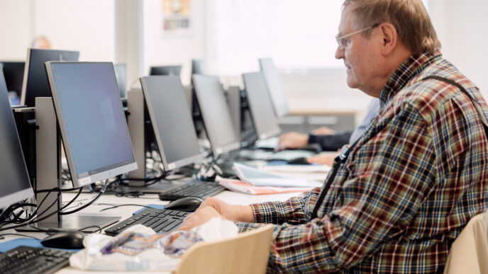 henkilö käyttämässä tietokonetta, taustalla lisää tietokoneita