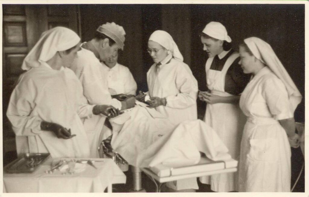 Lääkäri leikkaa potilasta sairaanhoitajien ympäröimänä mustavalkoisessa kuvassa.