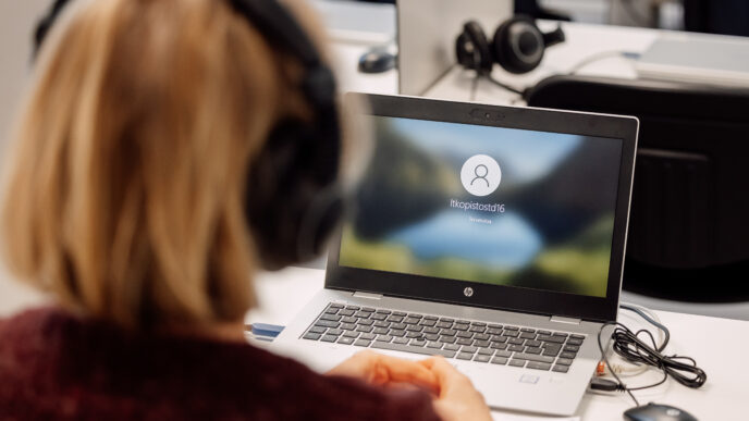 henkilö katsoo kannettavaa tietokonetta kohti, päässään kuulokkeet