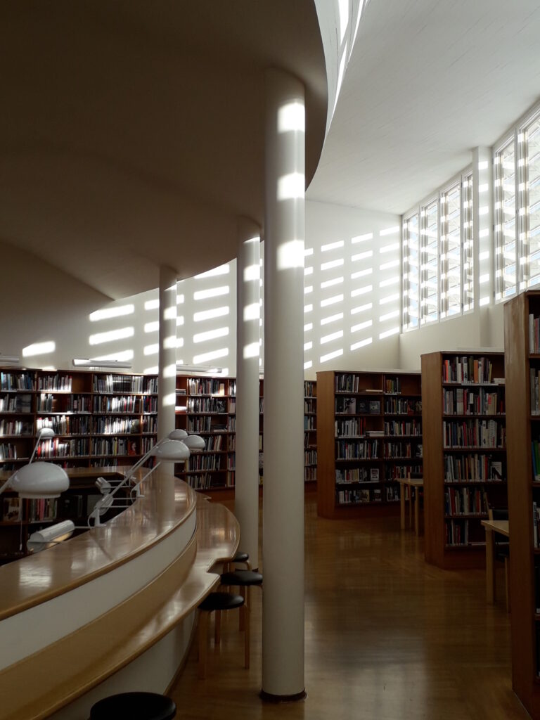 Aurinko paistaa säleikköjen välistä kirjasaliin.