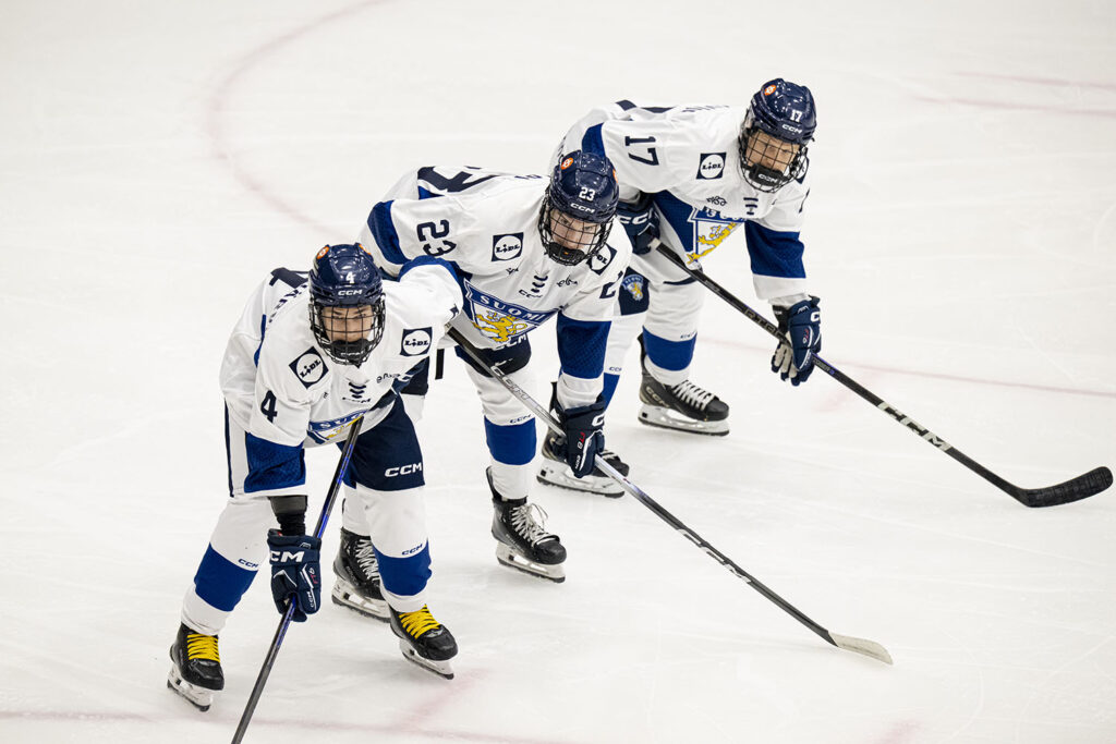Kolme jääkiekkoilijaa paikoillaan mailat jään pintaan asetettuina.