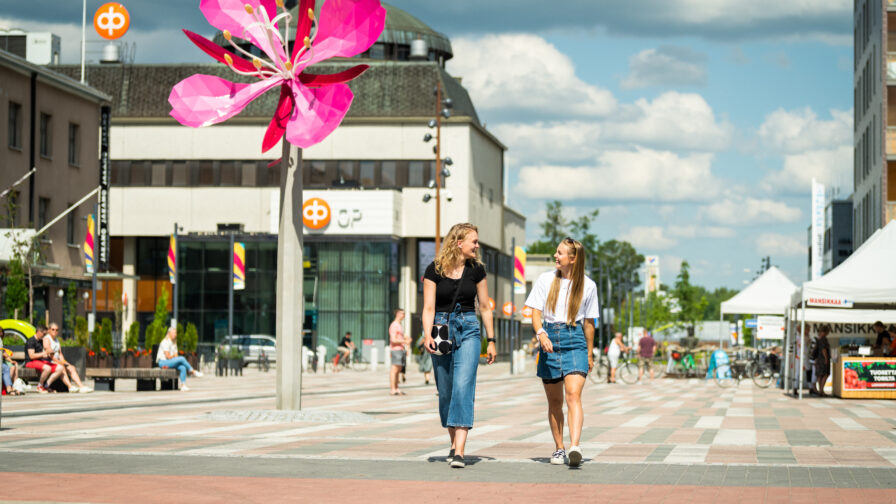 Kaksi nuorta henkilöä kävelee Keskustorilla. Taustalla Horsma-patsas.