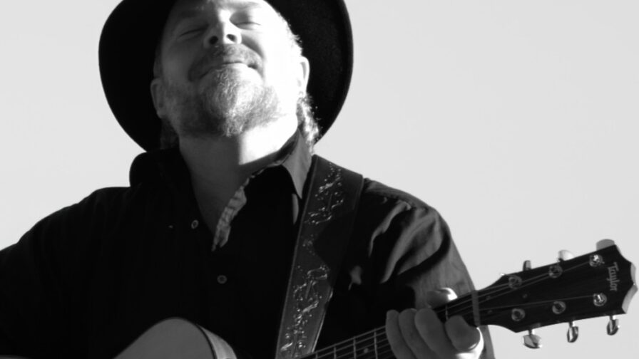 Mustavalkokusassa mies soittaa kitaraa