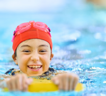 Lapsi ui uimalaudalla punainen lakki ja uimalasit päässä.