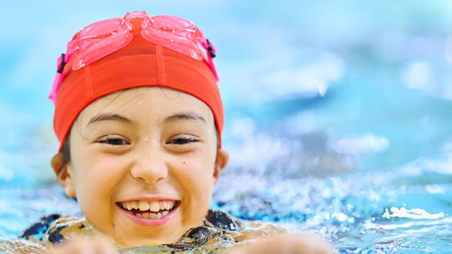 Lapsi ui uimalaudalla punainen lakki ja uimalasit päässä.
