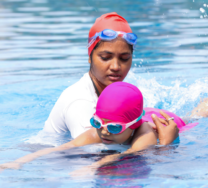 Aikuinen kannattelee lasta vedessä.