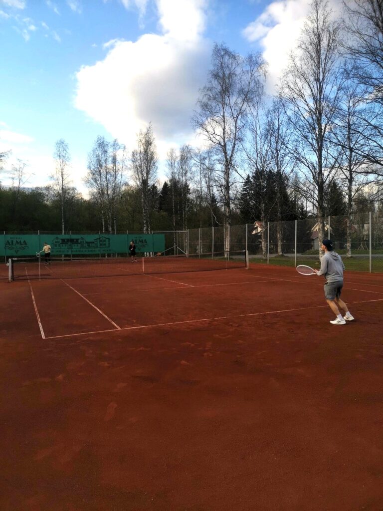 Tenniksen pelaajia punaisella massakentällä.