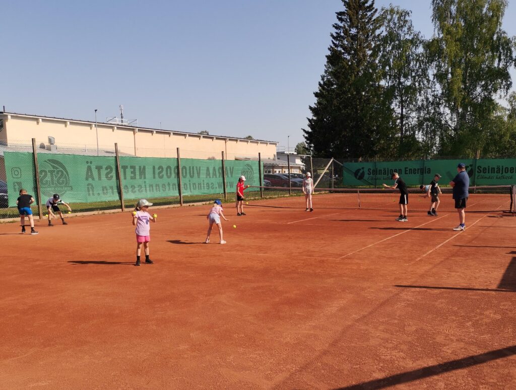 Tenniksen pelaajia punaisella massakentällä.