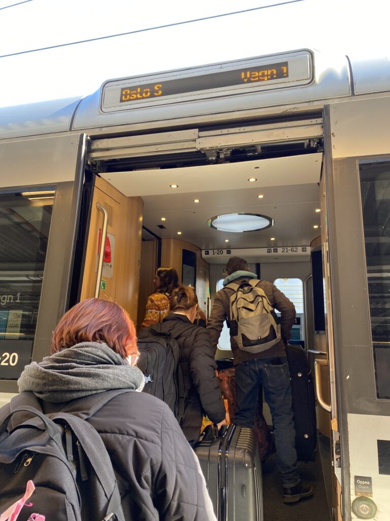 Ihmisiä nousemassa junaan, oviaukon yläpuolella lukee Oslo 1, vagn 1.
