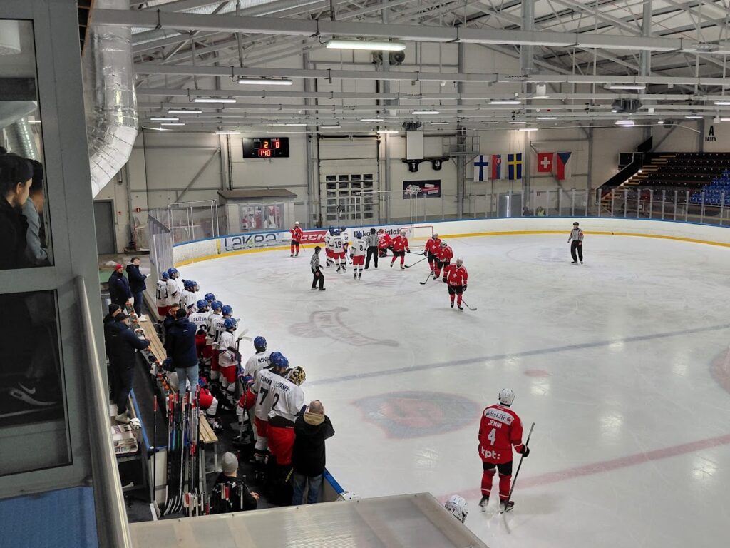 Jääkiekkoilijoita pelaamassa kaukalossa ja vaihtopenkillä seuraamassa tilannetta.