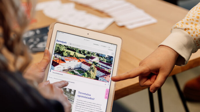 Henkilöt katsovat ja osoittavat älytablettia, jossa avoinna Seinäjoen kansalaisopiston nettisivut.