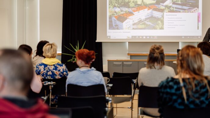 Henkilöitä istuu luentosalissa, edessä heijastettu Seinäjoen kansalaisopiston nettisivujen etusivu.