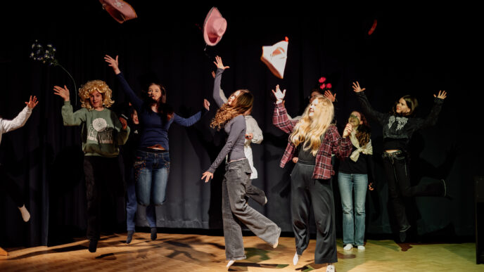 Henkilöitä teatterilavalla, heittävät hattujaan ilmaan