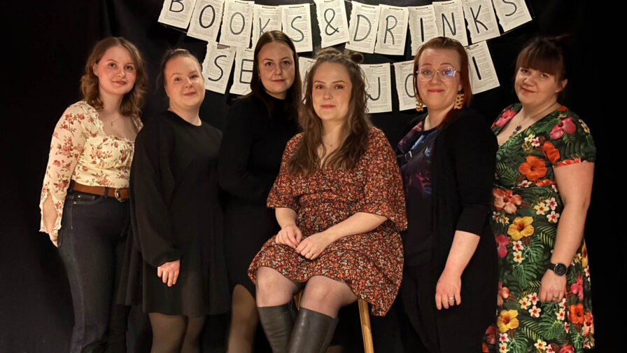 Kuusi naista poseeraavat mustalla taustalla. Naisten takana näkyy teksti: books & drinks Seinäjoki.