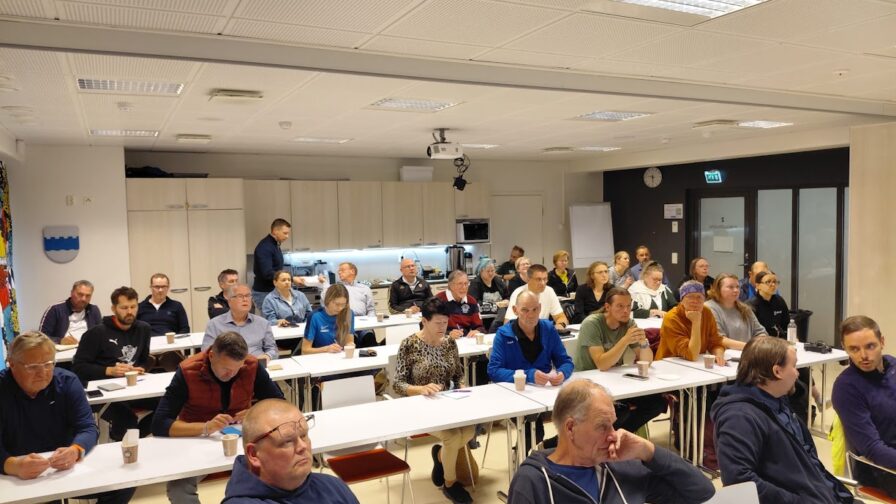 Ihmisiä kokoustilassa kuuntelemassa puhetta