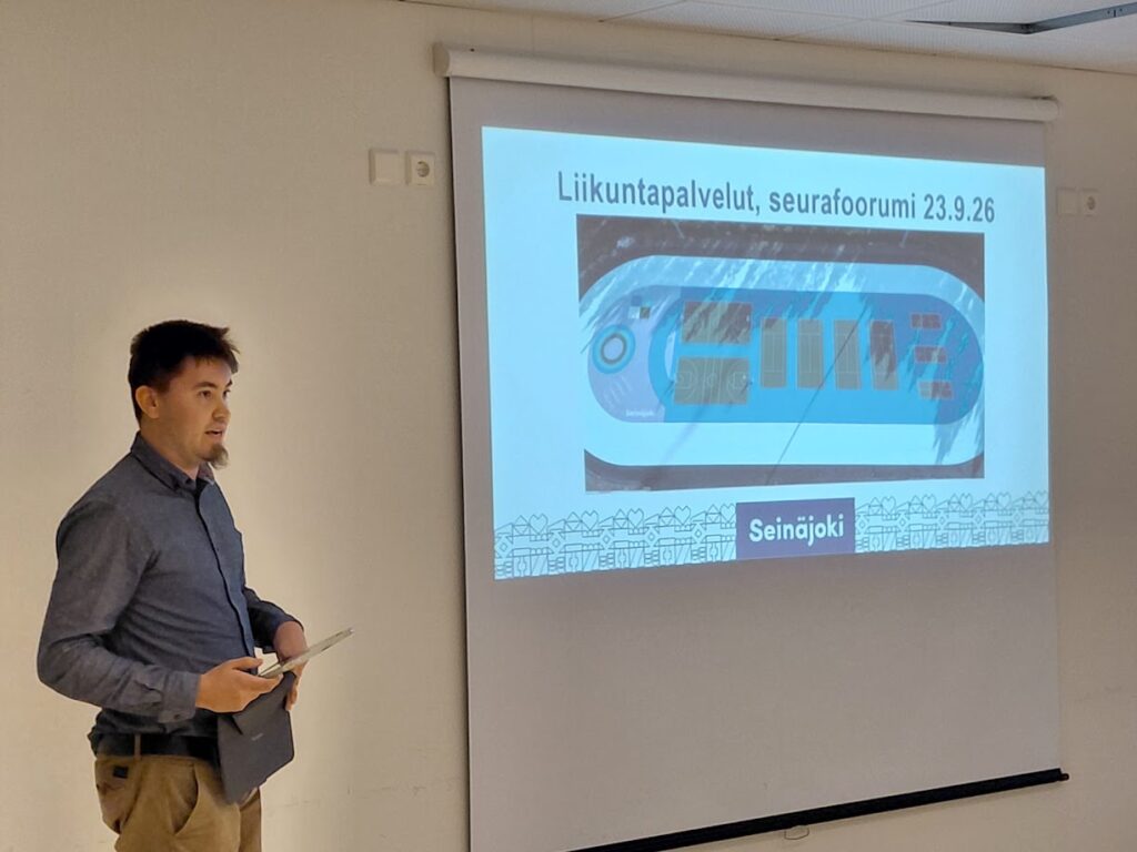 Henkilö puhumassa valkokankaan vieressä.